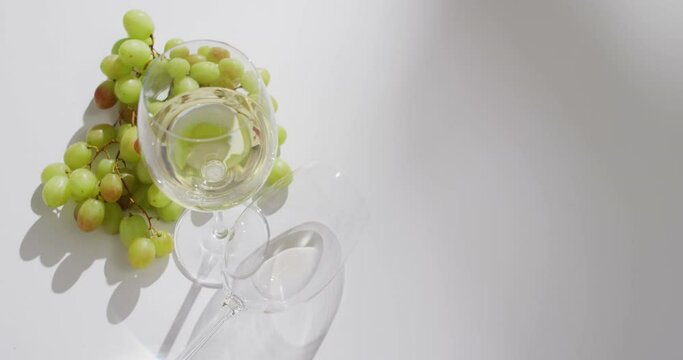 White wine glass and grapes lying on white surface with copy space