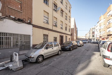 Obraz premium Facades of urban residential housing of modest construction in a street with cars parked in a row
