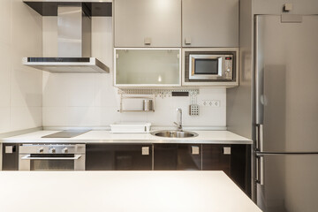 Open kitchen furnished with base units in gloss black, white countertop with aluminum edge and wall units in gray with integrated appliances in a study