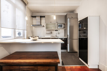Open kitchen furnished with base units in gloss black, white countertop with aluminum edge and wall units in gray with integrated appliances in a studio apartment