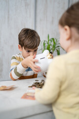Naklejka premium Siblings boy and girl small caucasian child brother and sister play at home with piggy bank saving money childhood investment insurance and finance concept copy space