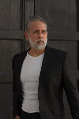 Attractive gray-haired man dressed in black suit walking downtown with black backpack