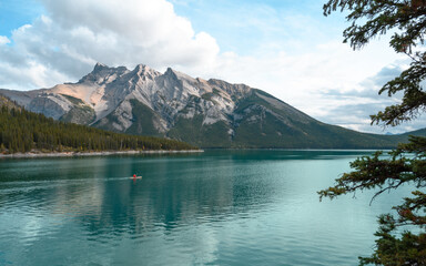 Panoramic image of a lake in Canada, in summer, with crystal blue water and snow on the mountains in the background. A canoe in the center.