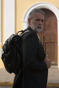 Attractive gray-haired man dressed in black suit walking downtown with black backpack