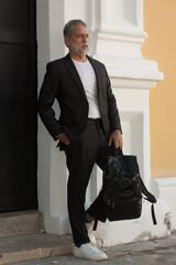 Attractive gray-haired man dressed in black suit walking downtown with black backpack