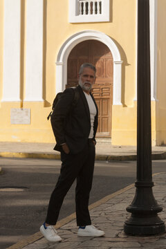 Attractive gray-haired man dressed in black suit walking downtown with black backpack