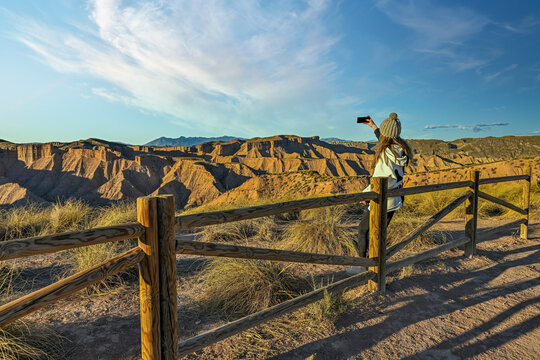 Girl observing the desert landscape, leaning on a wooden fence