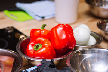 Red bell peppers and onions on a wooden kitchen table. Ingredients of raw food in metal bowls.