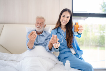 Smiling young nurse in hospital and health care center giving routine medications to happy and cheerful senior patient lying and sitting on bed while having a fun conversation