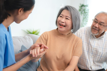 Fototapeta premium Smiling young nurse in uniform sitting with senior male and female couple at home assuring and building them in confidence about recovery in health