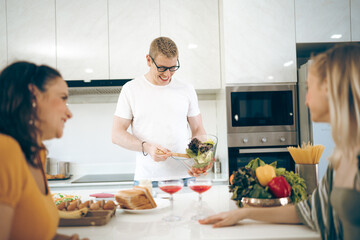 Cheerful family of young mother and father with their teenage daughter enjoying in modern kitchen while preparing healthy breakfast and juice while tasting food