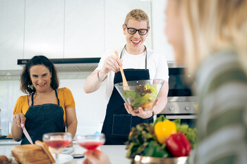 Cheerful family of young mother and father with their teenage daughter enjoying in modern kitchen while preparing healthy breakfast and juice while tasting food