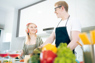 Cheerful family of young mother and father with their teenage daughter enjoying in modern kitchen while preparing healthy breakfast and juice while tasting food