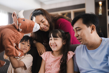 Cheerful and playful young Asian family with father along with mother and son and daughter sitting on couch and playing with rabbit stuff toy at home