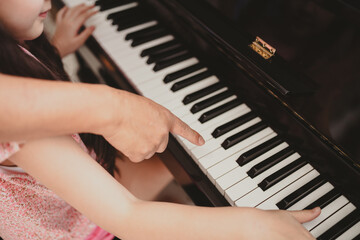 Cute and focused young little Asian girl practicing songs and melody with father and tutor while pressing white and black key and creating new music on piano as hobby and dedication at home
