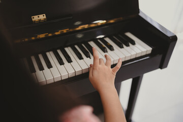 Cute and focused young little Asian girl practicing songs and melody while pressing white and black key and creating new music on piano as hobby and dedication at home