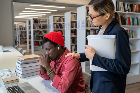 Supportive teacher-student relationships. Young woman tutor comforting upset African guy college student while preparing him for university test in library. Private tutoring concept