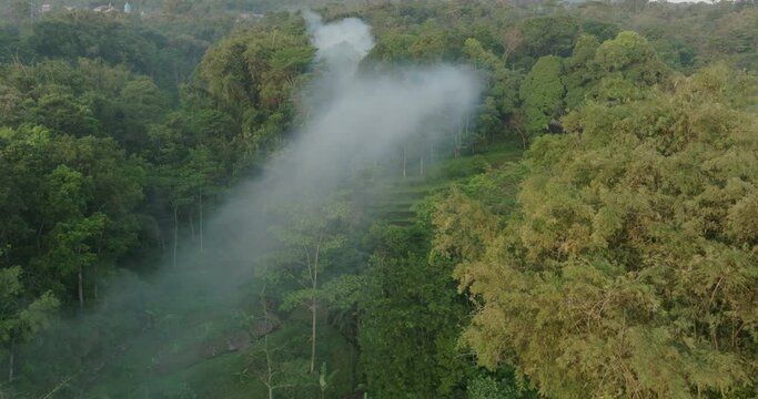 Aerial Forward Shot Of Smoke Spreading Over Tranquil Green Hill - Java, Indonesia