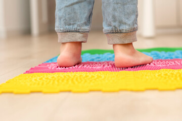 Health concept. A little boy stands with bare feet on a multi-colored orthopedic massage mat.