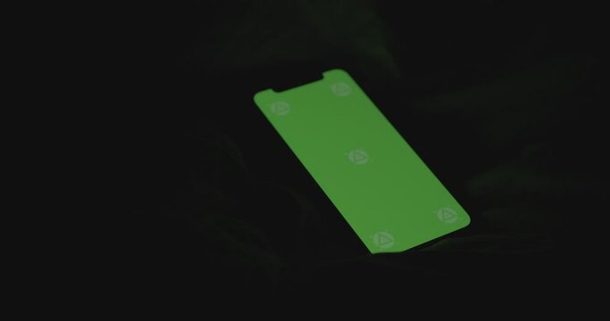Greenscreen smartphone resting on a duvet in the dark