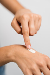 Girl applying hand moisturizer cream to protect skin from dryness in bedroom. Woman in bathrobe with hands moisturizing cream doing morning beauty routine.