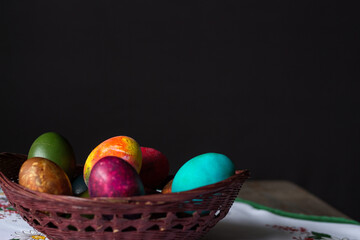 Fototapeta na wymiar Colored Easter eggs in a wooden basket on a white tablecloth at black background. Copy space.