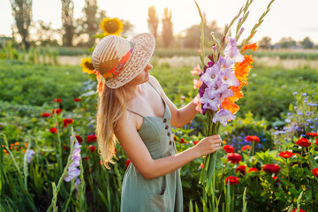 Portrait of young woman gardener enjoying bunch of fresh gladiolus in summer garden. Farmer picked...
