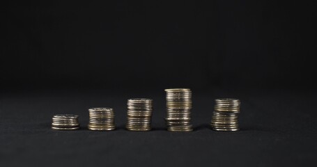 Stacks of coins stand on a black background. Five stacks of coins stand in a row on a black background. The concept of savings, poverty.