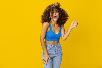 Woman with curly afro hair in a blue t-shirt on. yellow background signs with her hands, look into the camera, smile with teeth and happiness, copy space