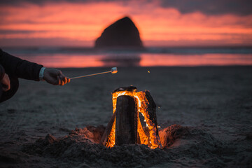 Man's hand with an marshmallow, Inviting campfire on Cape Kiwanda Beach with haystack rock during...