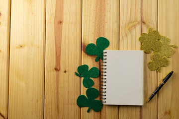 Image of green clover and white notebook with copy space on wooden background