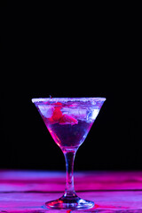 Glass with cocktail and diverse fruits in neon light with copy space over black background