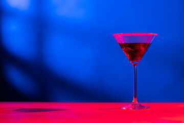 Glass with cocktail and diverse fruits in neon light with copy space over blue background