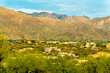 Fototapeta na wymiar Towering moutains in the sonora desert overlooking houses in a ravine with adobe styles on homes in natural environment