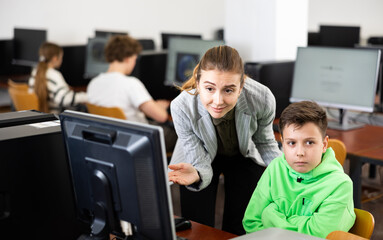 Obraz premium Female teacher and her student, young boy, looking at monitor of PC during computer science lesson.