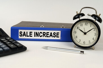 On a white surface, an alarm clock calculator and a folder with the inscription - SALE INCREASE
