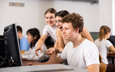 Two positive classmates rejoicing solving of task of computer science with male teen while he is using the pc in the class