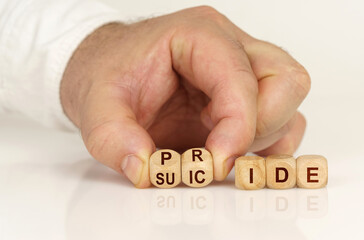 On the reflective surface in the hands of a man are cubes with the inscription - Pride or suicide