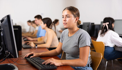 Woman sitting at desk in computer class and using PC, learning to use software.