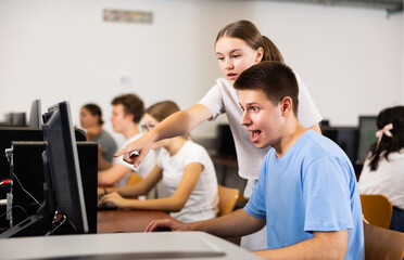 Positive young boy and girl using personal computer together, enjoying computer game.