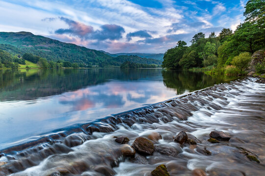 The River Rothay flowing over the weir at Grasmere Lake towards Rydal and on to Windermere in the Lake District National Park. A lovely morning sky over the Barrowdale fells in the distance.