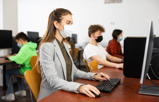 Concentrated Young Woman In Protective Mask Studying In Computer Lab In Public Library During Coronavirus Pandemic..