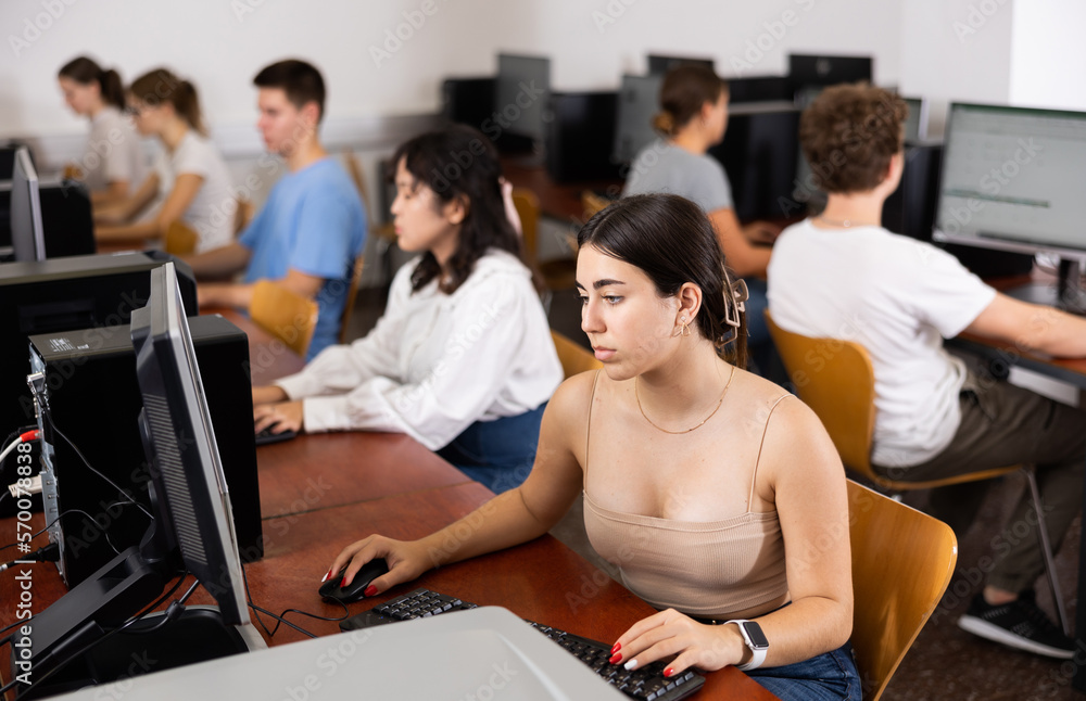 Poster smart latin female teenager learning computer science while she is using a pc in the computer classr