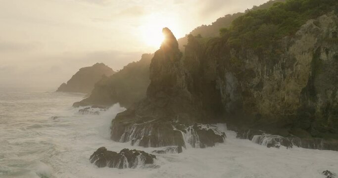 Aerial Beautiful View Of Rock Formations Against Clouds, Drone Flying Backwards Over Wavy Sea - Java, Indonesia