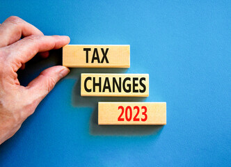 Tax changes 2023 symbol. Concept words Tax changes 2023 on wooden blocks on a beautiful blue table blue background. Businessman hand. Business Tax changes 2023 concept. Copy space.