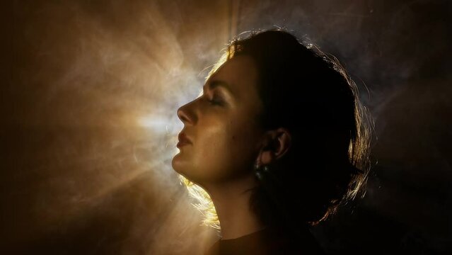 Lady half face with elegant makeup and hairdo poses against steam cloud lit by sun back light on black closeup slow motion
