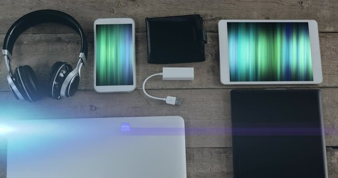 Animation of light trails over technological devices with colorful moving shapes on screen on desk