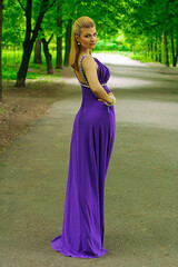 blonde beautiful natural girl with blonde hair in a lilac dress in nature, in the park, in the garden by a tree, with makeup and hairstyle without a bra