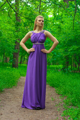 blonde beautiful natural girl with blonde hair in a lilac dress in nature, in the park, in the garden by a tree, with makeup and hairstyle without a bra