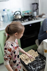 Little girl helping her grandmother with cooking russian dumplings at home
